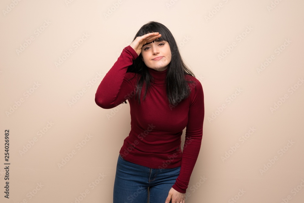 Young woman with red turtleneck looking far away with hand to look something Young woman with red turtleneck looking far away with hand to look something