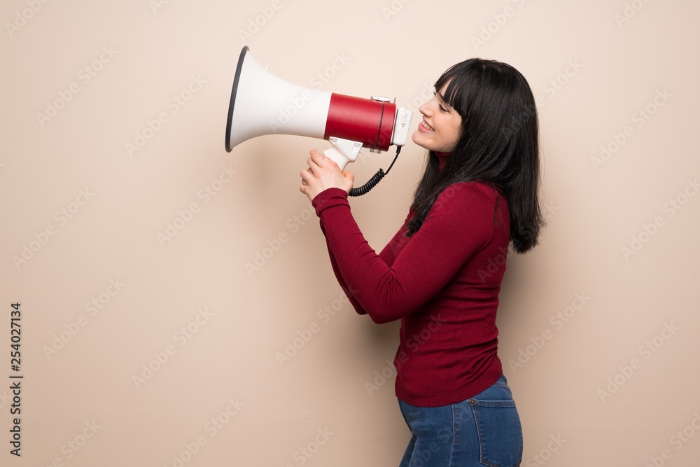 Young woman with red turtleneck shouting through a megaphone to announce something in lateral position Young woman with red turtleneck shouting through a megaphone to announce something in lateral position