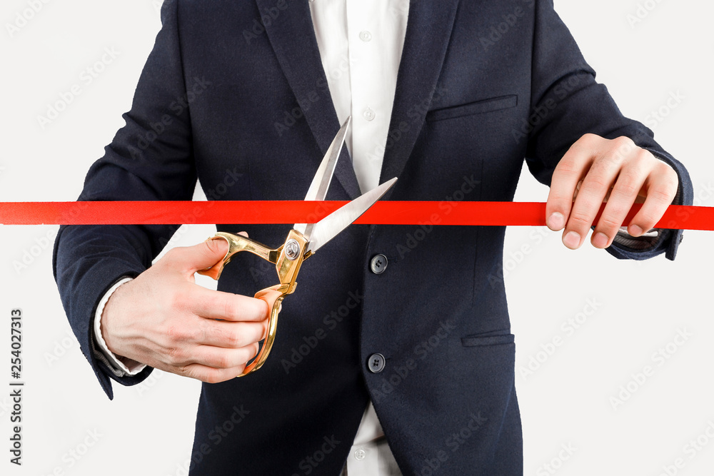 Businessman cutting red ribbon with pair of scissors close up