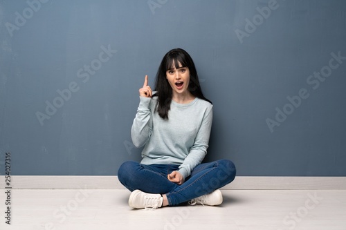 Woman sitting on the floor thinking an idea pointing the finger up