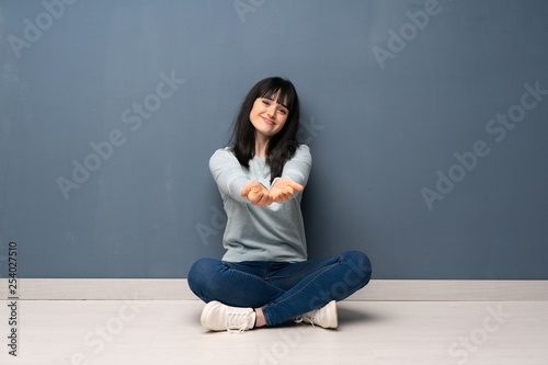 Woman sitting on the floor holding copyspace imaginary on the palm to insert an ad