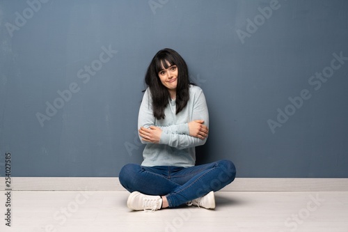 Woman sitting on the floor making doubts gesture while lifting the shoulders