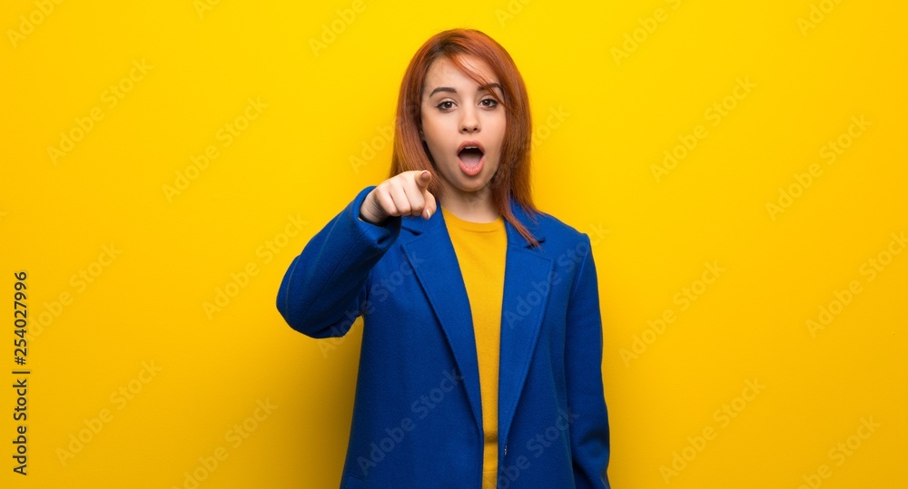Young redhead woman with trench coat surprised and pointing front Young redhead woman with trench coat surprised and pointing front