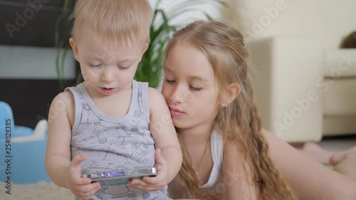 Adorable little brother and sister using digital tablet, smiling and looking happy. Brother and sister having fun at home.