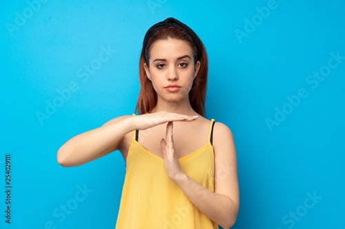 Young redhead woman over blue background making time out gesture