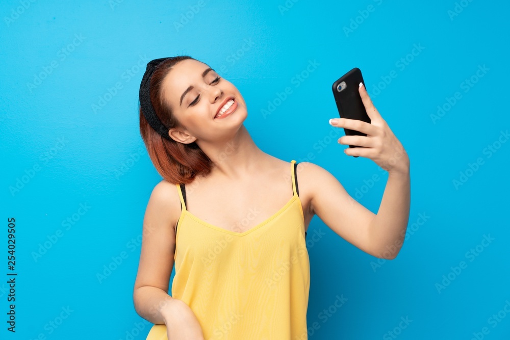 Young redhead woman over blue background making a selfie Young redhead woman over blue background making a selfie
