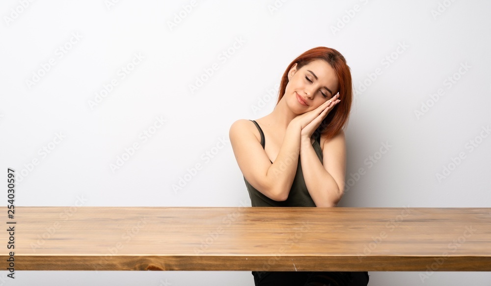Young redhead woman at desk making sleep gesture in dorable expression Young redhead woman at desk making sleep gesture in dorable expression