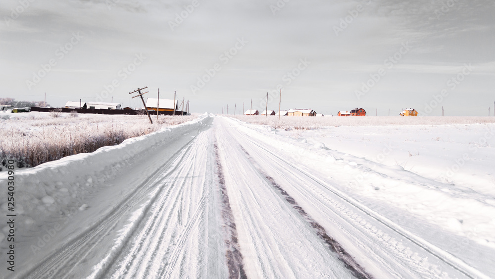 winter road. snow and ice. tire tracks. remote place, farm houses and fields covered with snow. Photo in gray tones winter road. snow and ice. tire tracks. remote place, farm houses and fields covered with snow. Photo in gray tones