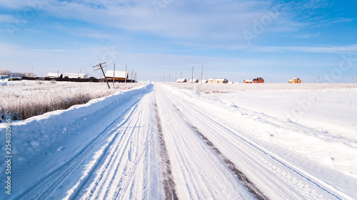 winter road. snow and ice. tire tracks. remote place, farm houses and fields covered with snow. blue sky, colorful photo.