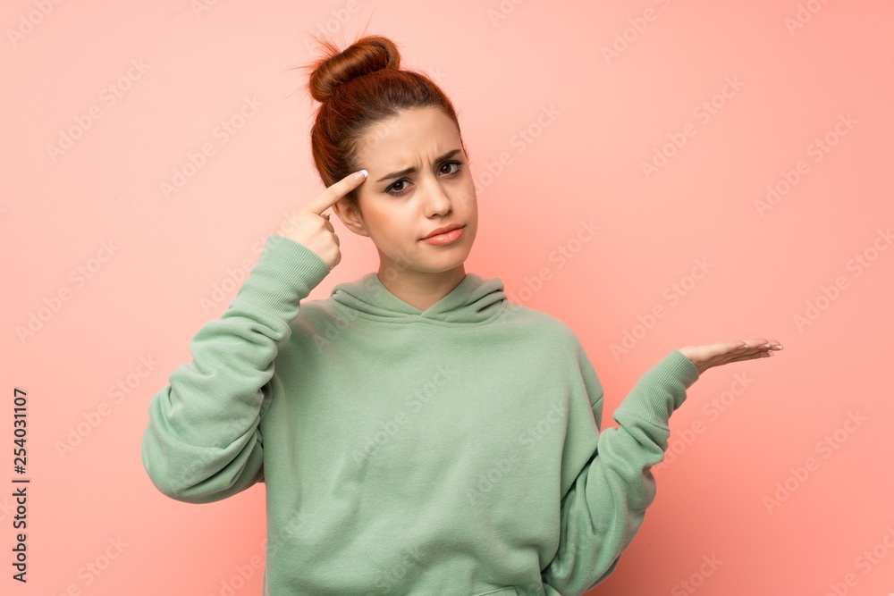 Young redhead woman with sweatshirt making the gesture of madness putting finger on the head