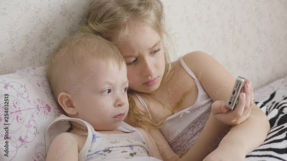Adorable little brother and sister using digital tablet, smiling and looking happy. Brother and sister having fun at home. Adorable little brother and sister using digital tablet, smiling and looking happy. Brother and sister having fun at home.