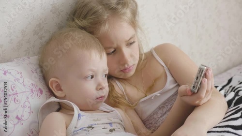 Adorable little brother and sister using digital tablet, smiling and looking happy. Brother and sister having fun at home.