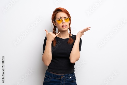 Young redhead woman over white wall making phone gesture and doubting