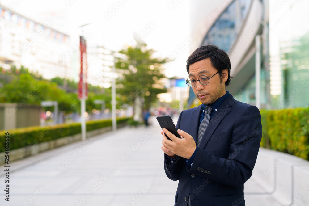 Asian businessman using phone in the city outdoors Asian businessman using phone in the city outdoors
