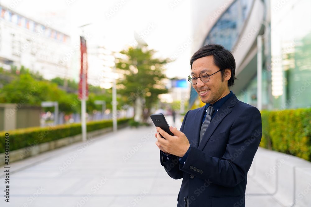 Happy Asian businessman using phone in the city outdoors Happy Asian businessman using phone in the city outdoors