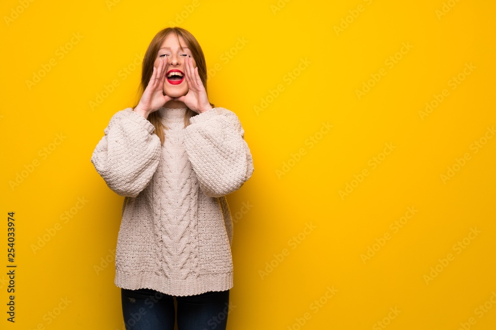 Redhead woman over yellow wall shouting and announcing something