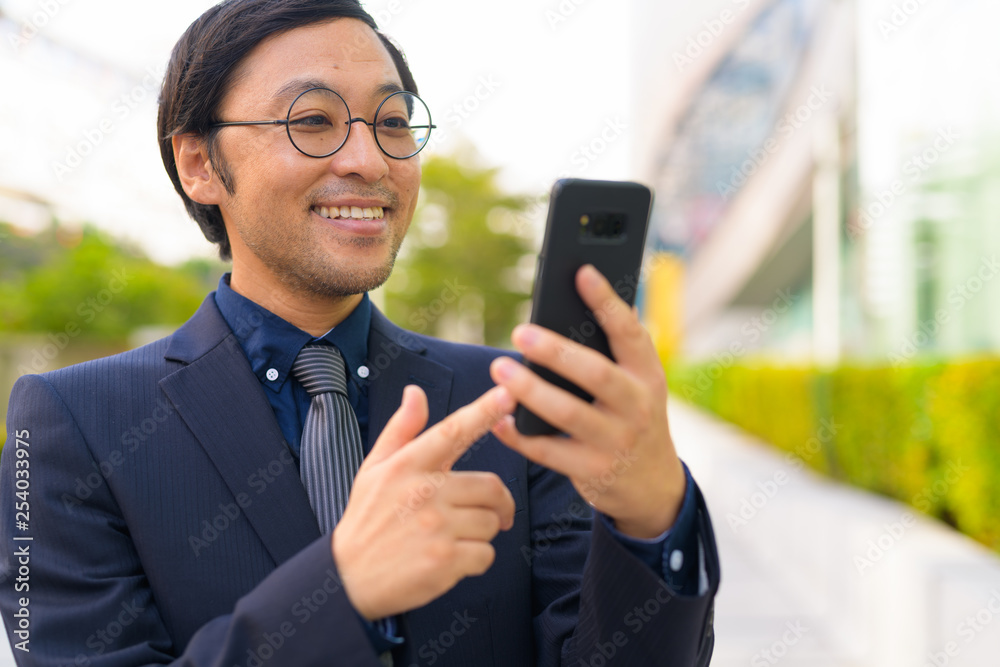 Face of happy Asian businessman using phone in the city outdoors Face of happy Asian businessman using phone in the city outdoors