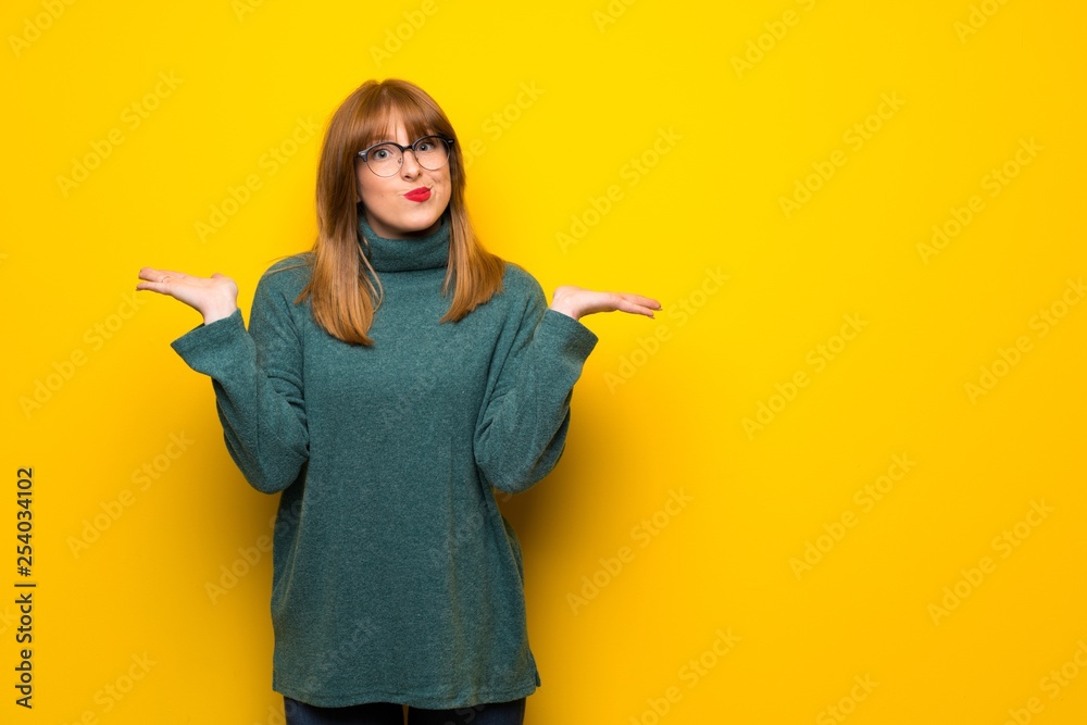 Woman with glasses over yellow wall having doubts while raising hands and shoulders Woman with glasses over yellow wall having doubts while raising hands and shoulders