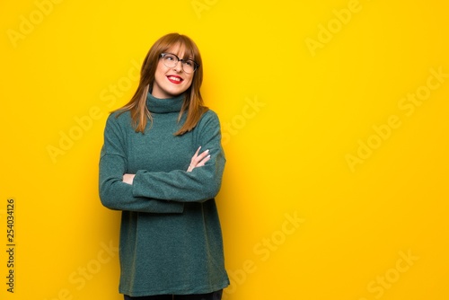 Woman with glasses over yellow wall looking up while smiling © luismolinero