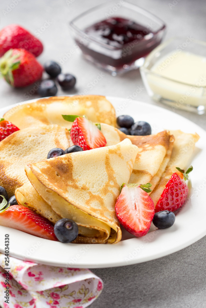 Thin pancakes with strawberries and blueberries, jam, condensed milk, delicious Breakfast. Russian traditional dessert for Shrovetide celebration (maslenitsa). French crepes Thin pancakes with strawberries and blueberries, jam, condensed milk, delicious Breakfast. Russian traditional dessert for Shrovetide celebration (maslenitsa). French crepes