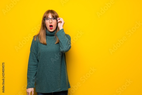 Woman with glasses over yellow wall with glasses and surprised © luismolinero