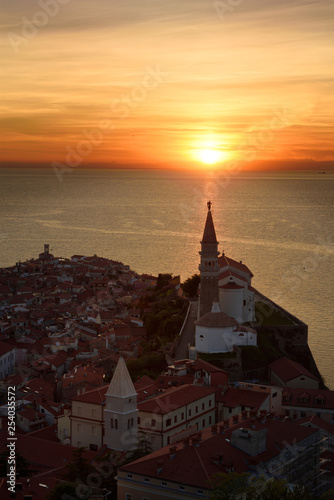 Setting sun on the Adriatic Sea behind Archangel Michael on top of belfry of St George's Cathedral of Piran Slovenia