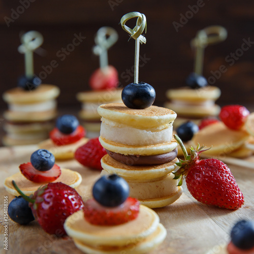 Fruit, berry and pancake canapes on white wooden table