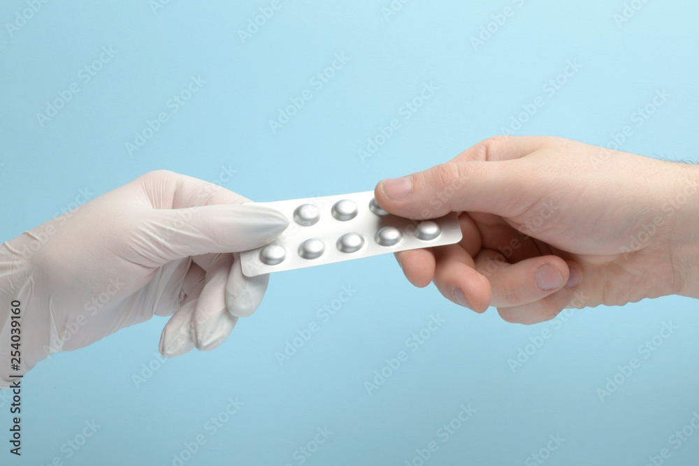 Hand in white latex glove holding assorted pill blisters, take it, on blue background Hand in white latex glove holding assorted pill blisters, take it, on blue background