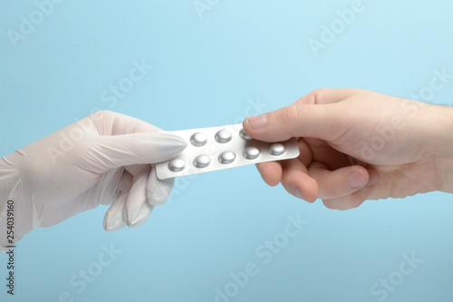 Hand in white latex glove holding assorted pill blisters, take it, on blue background