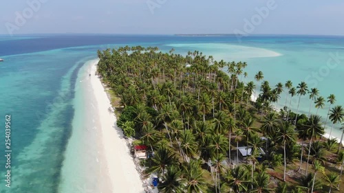 Aerial view of a narrow island near Tawi Tawi, Philippines. Small homes on a tiny strip of land surrounded by bright white sand beach and warm clear ocean. Drone slide right. photo