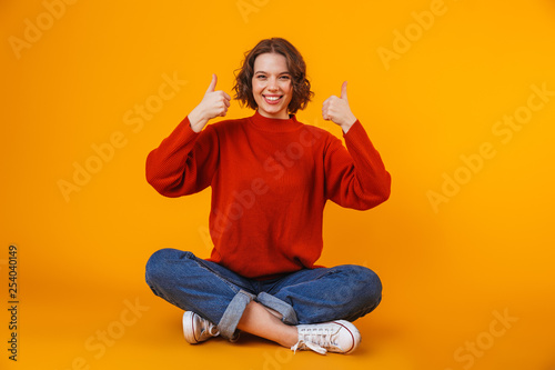 Emotional young pretty woman posing isolated over yellow wall background showing thumbs up. © Drobot Dean