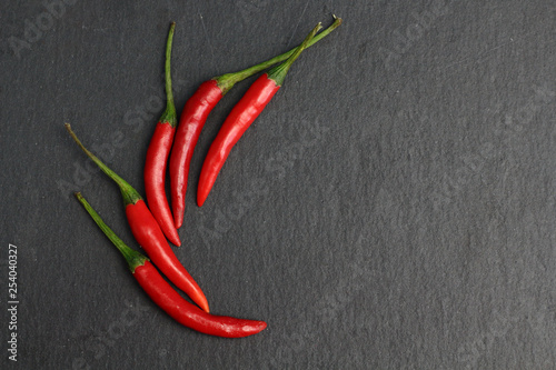 Group of hot spice red chilli fresh cayenne pepper on a black graphite slate stone surface. Natural vegeterian diet organic vegetable. Dark food foto