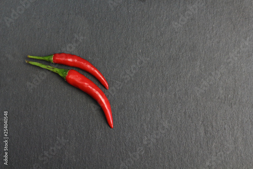 Two hot spice red chilli fresh cayenne pepper on a black graphite slate stone surface. Natural vegeterian diet organic vegetable. Dark food foto