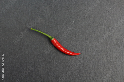 One sharp hot spice red chilli fresh cayenne pepper on a black graphite slate stone surface. Natural vegeterian diet organic vegetable. Dark food foto