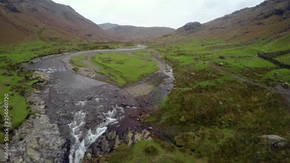 Aerial pull back through low altitude valley floor green landscape over fast flowing river into waterfall off side of cliff. Aerial pull back through low altitude valley floor green landscape over fast flowing river into waterfall off side of cliff.