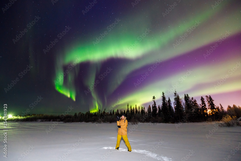 Man Traveler in yellow jacket with camera on background of northern lights