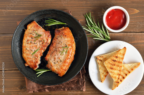 Fried pork steaks in frying pan, toast and tomatoes sauce