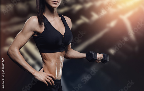 At center of frame is muscular female body with dumbbells in hand