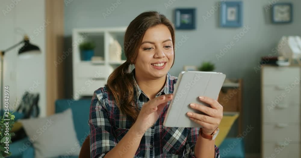 Portrait shot of the attractive young Caucasian woman sitting at home and scrolling on the tablet computer. Portrait shot of the attractive young Caucasian woman sitting at home and scrolling on the tablet computer.