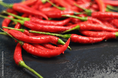 A lot of sharp hot spice red chilli cayenne pepper with wet drops of freshness water dew on a black graphite slate stone surface. Natural vegeterian diet organic vegetable. Dark food foto