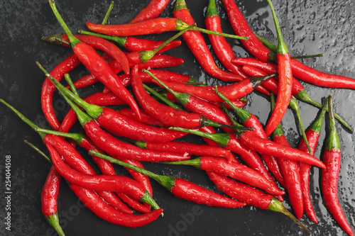 A lot of sharp hot spice red chilli cayenne pepper with wet drops of freshness water dew on a black graphite slate stone surface. Natural vegeterian diet organic vegetable. Dark food foto