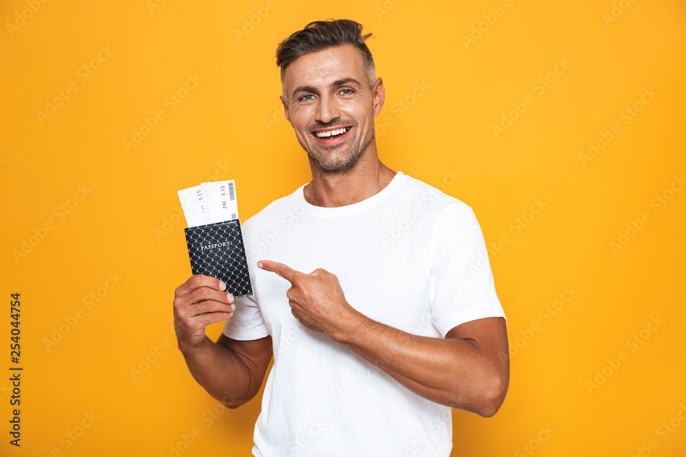 Image of joyous man 30s in white t-shirt holding passport and travel tickets Image of joyous man 30s in white t-shirt holding passport and travel tickets