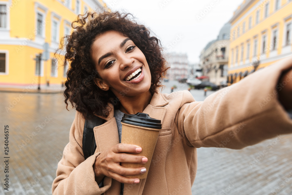 Fototapeta premium Cheerful young african woman wearing coat walking