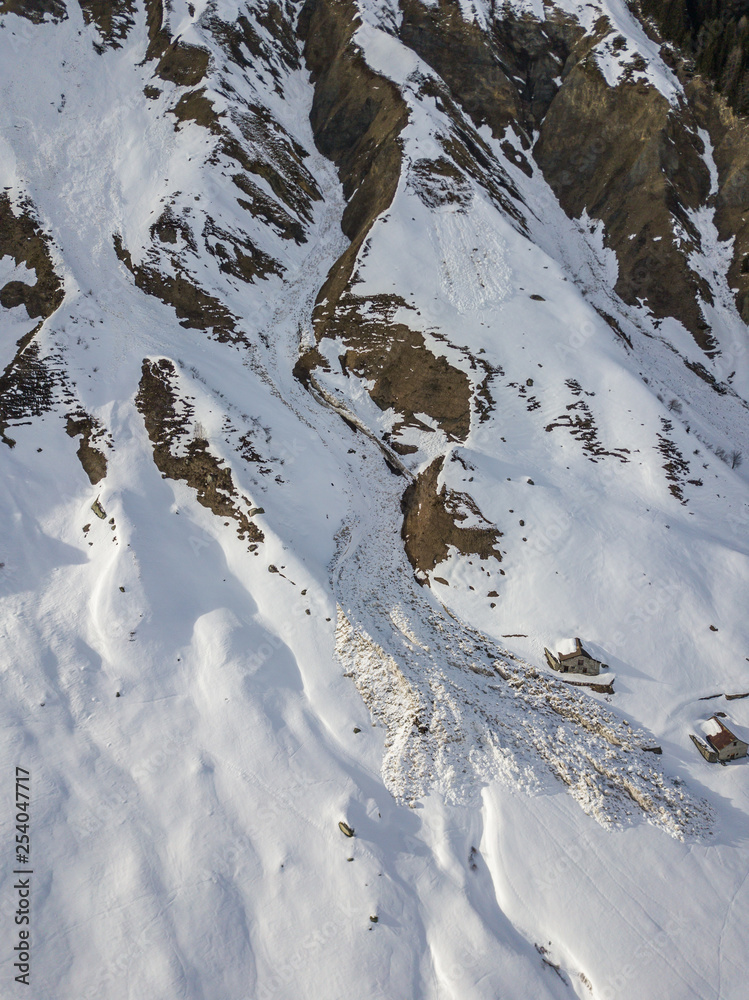 Aerial view of snow avalanche on mountain slope. Wet snow in spring sliding downhill.