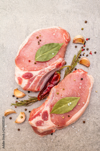 Raw pork steak with spices and dried herbs. Salt, garlic, hot pepper, rosemary, bay leaf on a stone background, top view, close up.