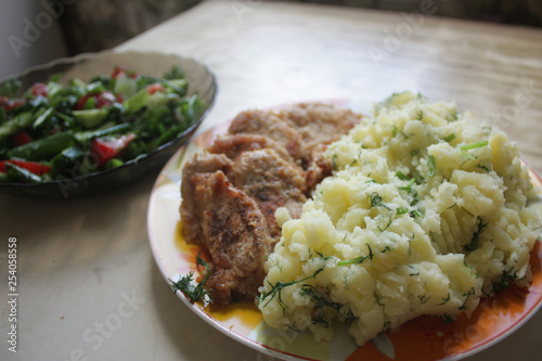 Dish consisting of fried meat and boiled potatoes and cucumber salad with green onions and tomatoes.