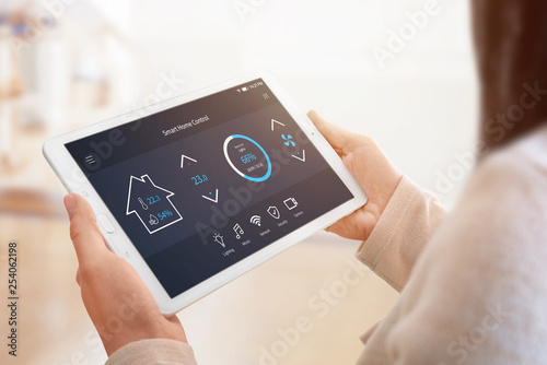 Modern home control app with flat interface on tablet display. Woman holding tablet. Sun light in background. Close-up.
