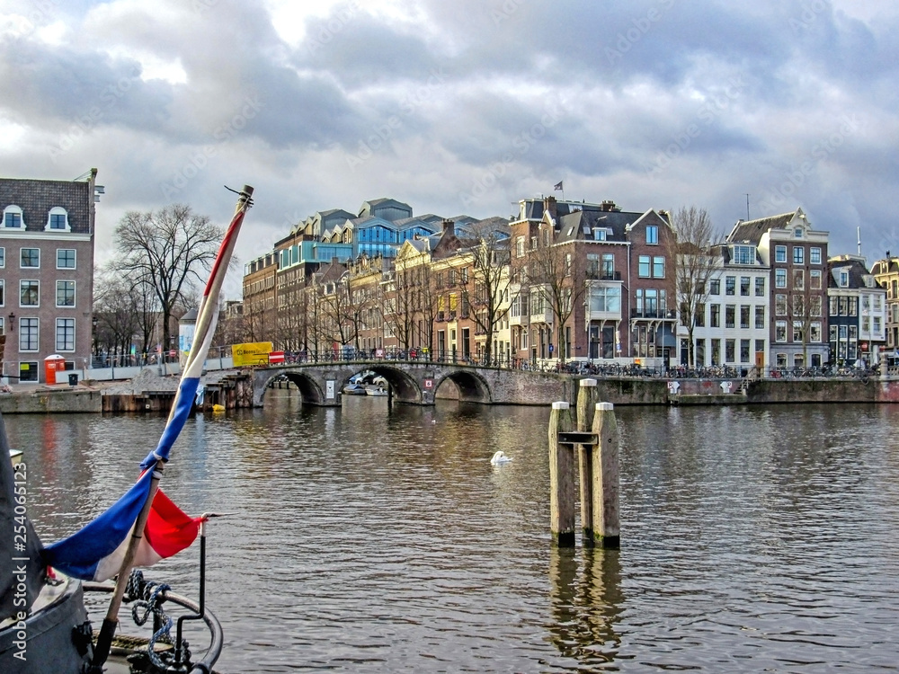 Dutch flag on the boat with bridge and Amsterdam famous duch traditional Flemish brick buildings