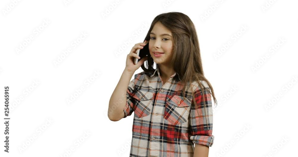 Caucasian cute little teenager girl in a motley blouse talking on the phone cheerfully and smiling on the white screen back. Caucasian cute little teenager girl in a motley blouse talking on the phone cheerfully and smiling on the white screen back.