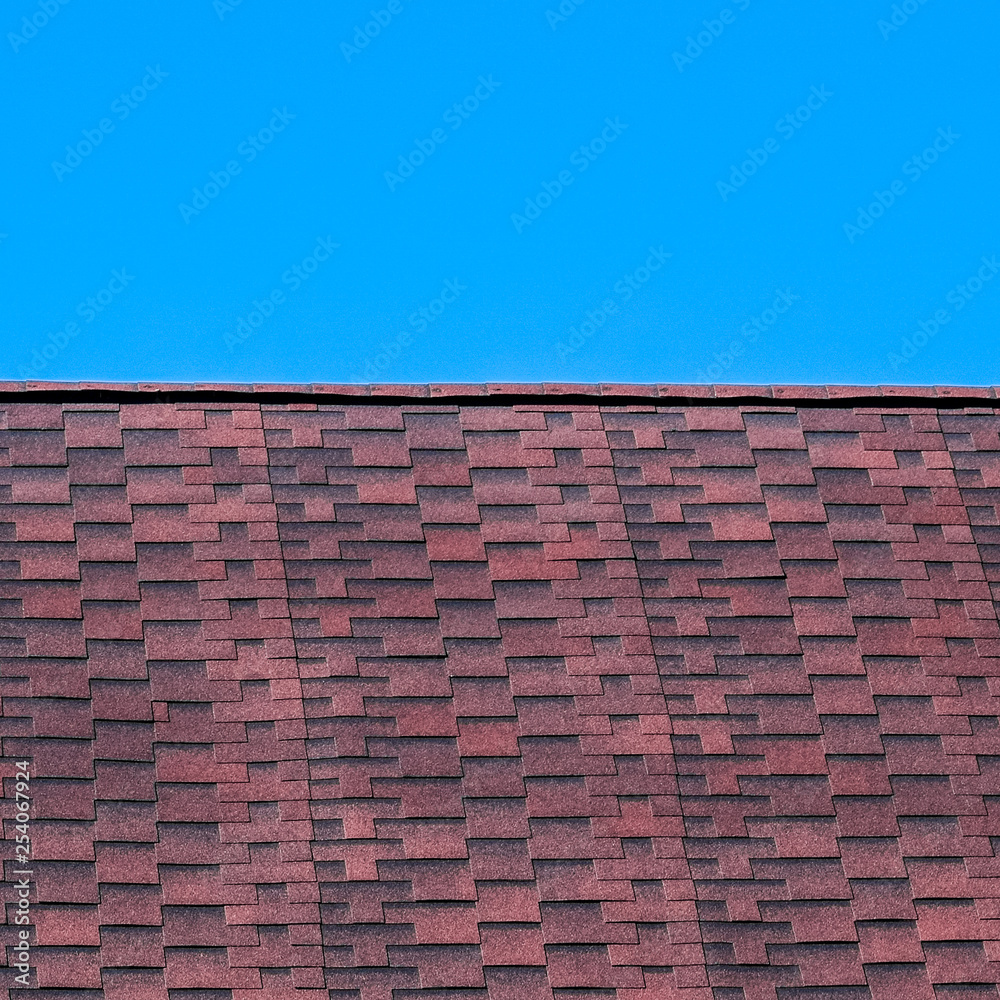 Roof from multi-colored bituminous shingles. Patterned bitumen shingles. Bituminous burgundy roof. Roof from multi-colored bituminous shingles. Patterned bitumen shingles. Bituminous burgundy roof.